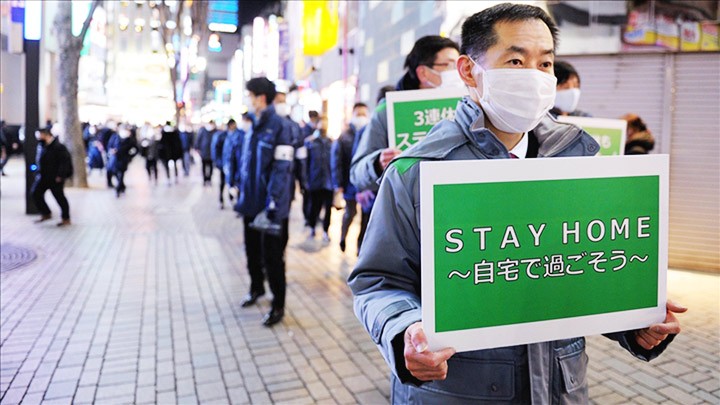 Một nhân viên y tế Nhật Bản cầm tấm biển đề nghị người dân nên ở nhà. Ảnh: ANADOLU AGENCY